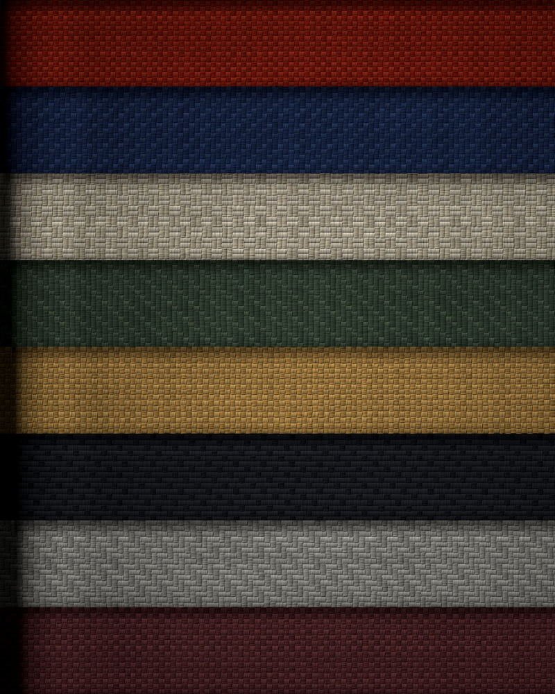 Folded lengths of dyed cloth stacked edge-on in red, navy, ecru, green, ochre, black and grey.
