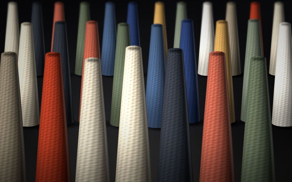 Rows of cross-wound yarn cones in ecru, indigo, madder and olive standing on the creel floor.
