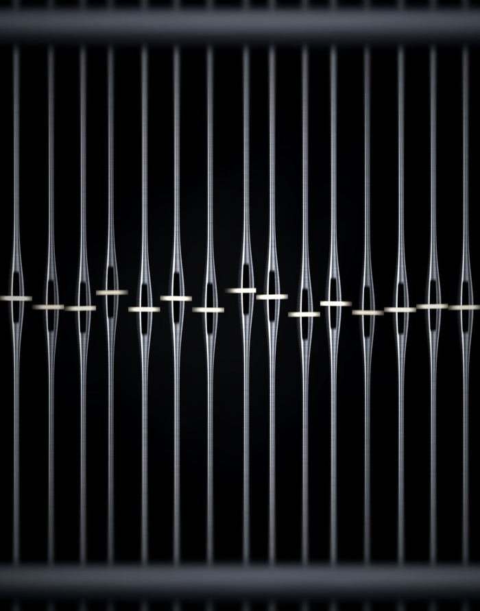 Steel heddles hanging in a harness frame, each eye carrying a single warp end.